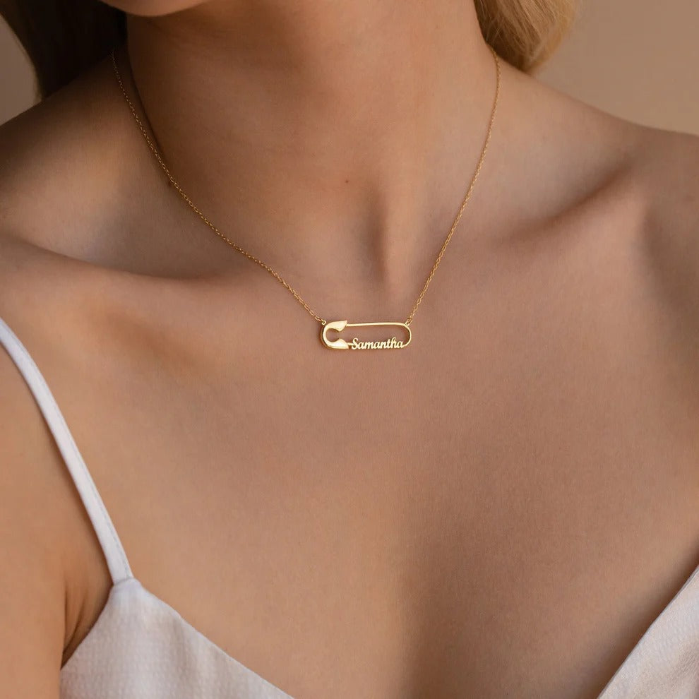 Gold necklace with a name pendant on a person wearing a white top.