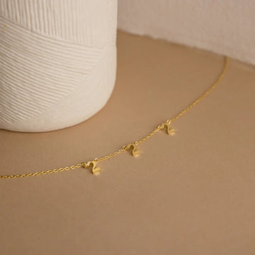 Gold necklace with heart pendants on a beige surface