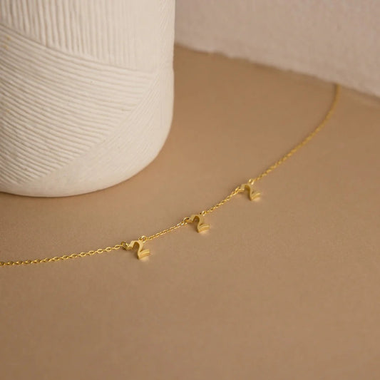 Gold necklace with heart pendants on a beige surface