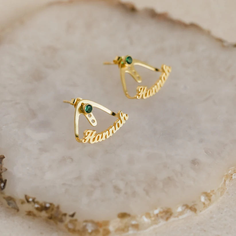 Gold earrings with green gemstones on a textured beige surface