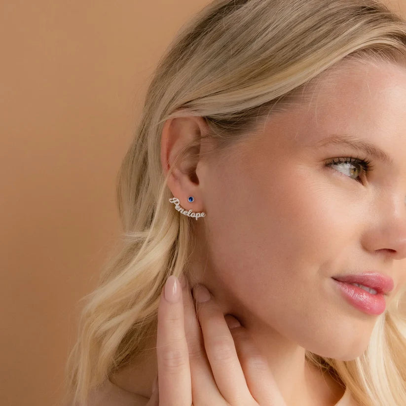 Close-up of a woman wearing an earring with 'Forever' text on a beige background