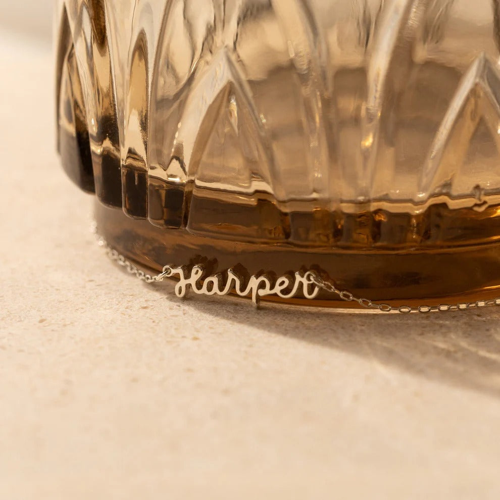 Gold necklace with 'Harper' pendant on a textured surface