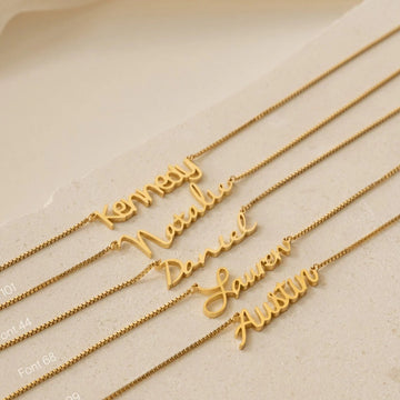Gold name necklaces on a beige surface