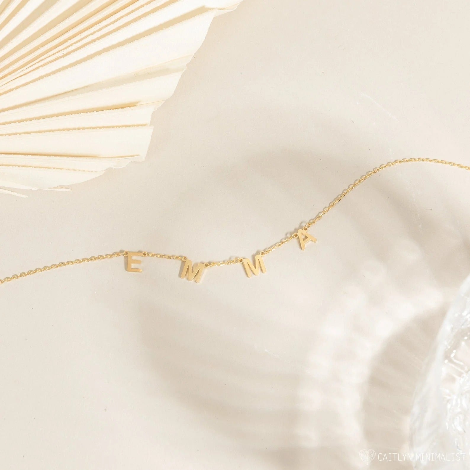 Gold necklace with 'EMMA' letters on a white fabric background