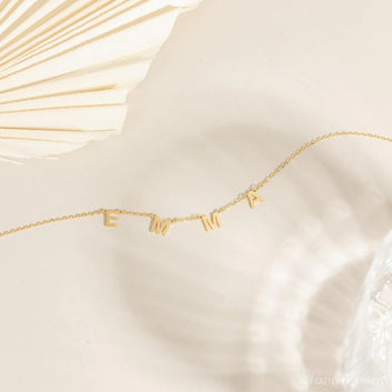 Gold necklace with 'EMMA' letters on a white fabric background