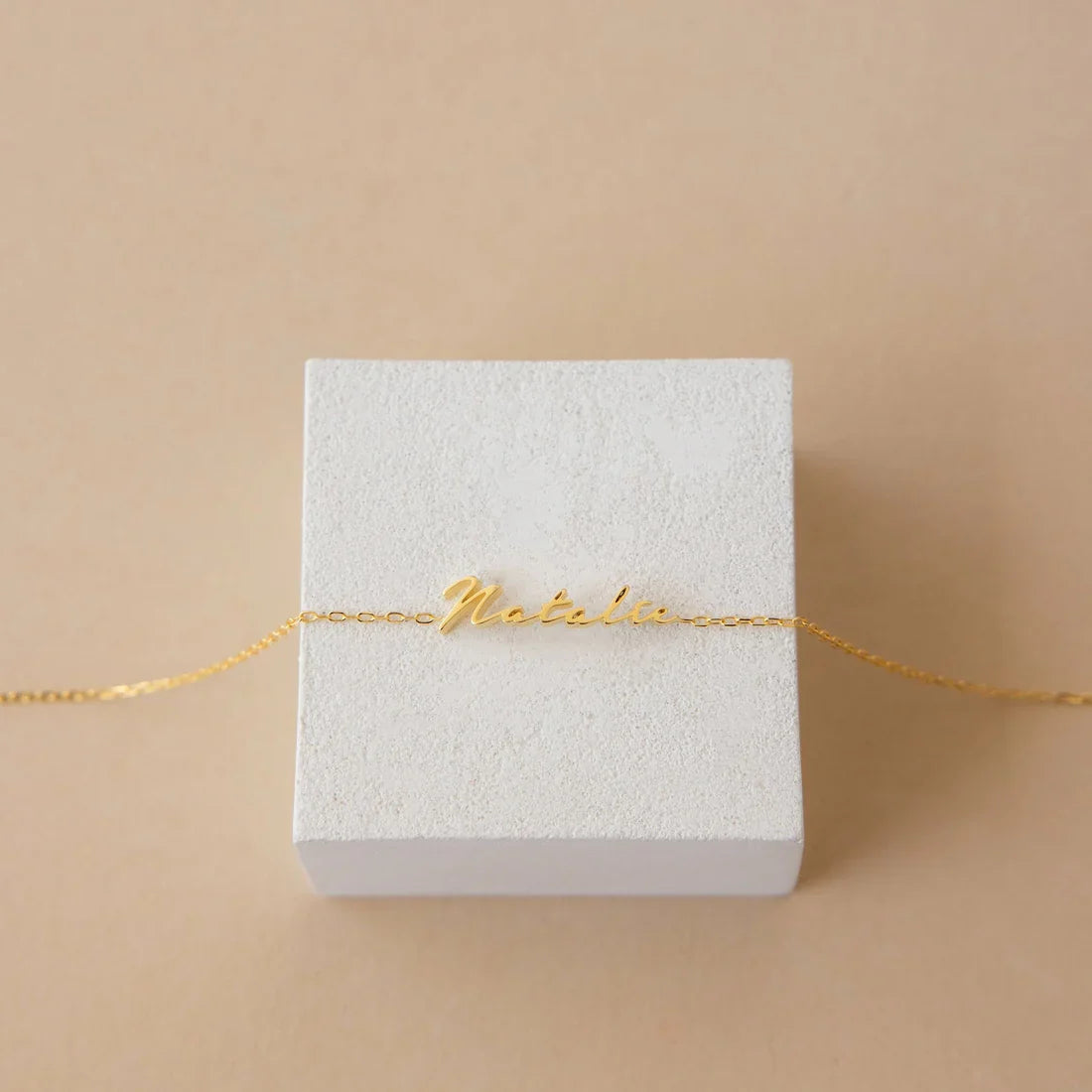Gold bracelet on a white box with 'Motel' engraving against a beige background