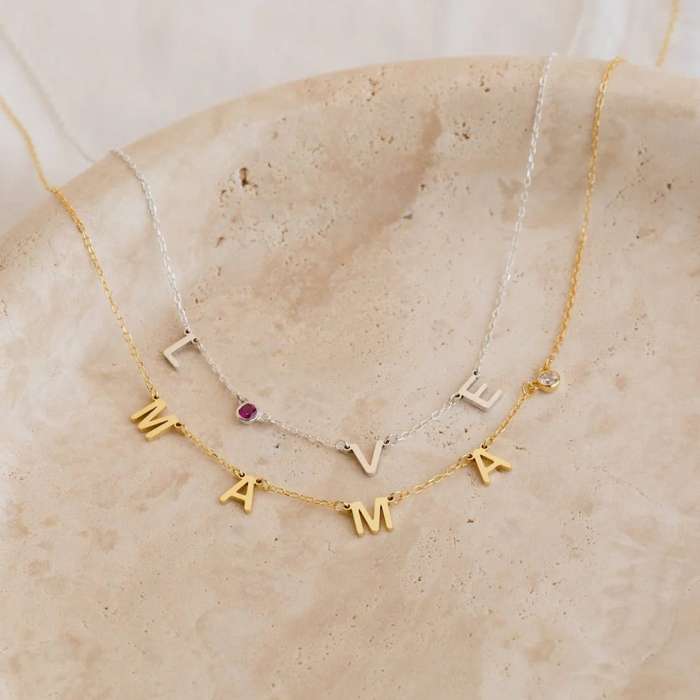 Two gold necklaces with letter pendants on a beige stone surface