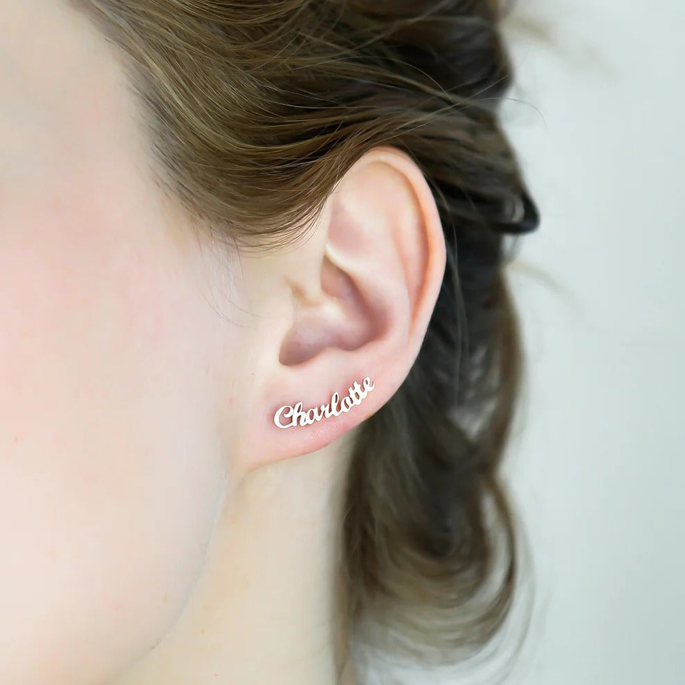Earring with 'Charlotte' text worn by a person with a blurred background