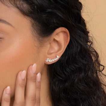 Close-up of an ear wearing a 'Hannah' earring with a hand touching the cheek against a beige background