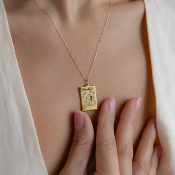 Gold necklace with a rectangular pendant on a person's neck, close-up view.