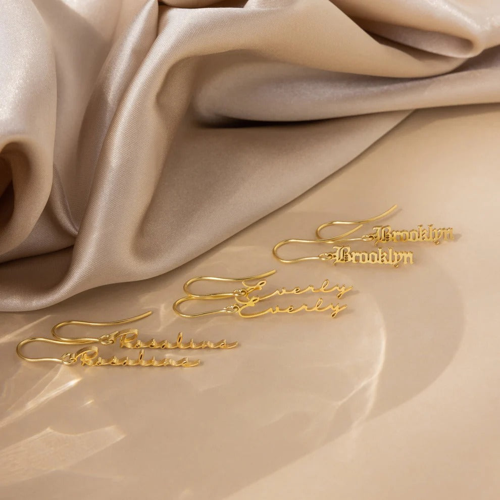 Gold earrings with 'Brooklyn' branding on beige fabric