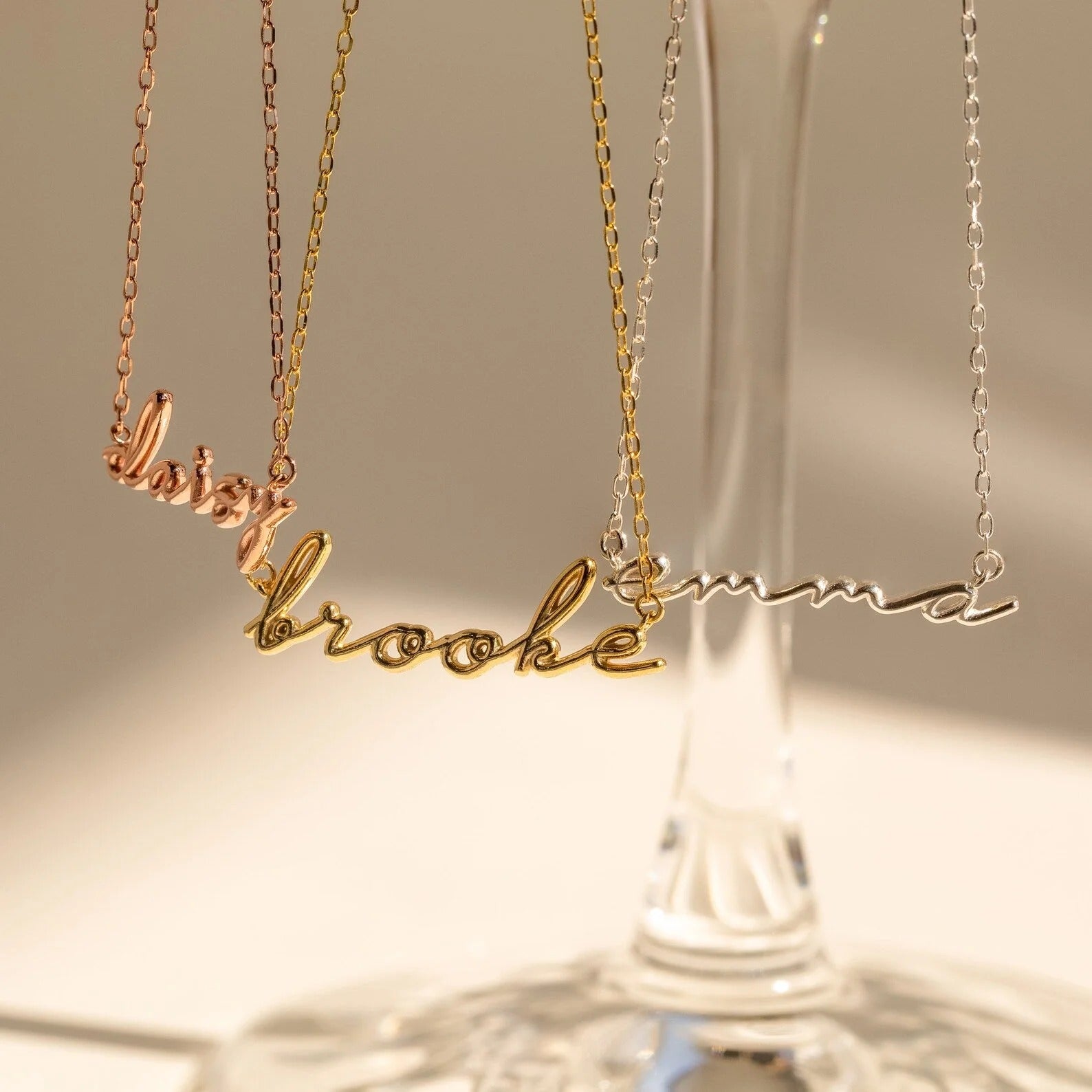 Three gold name necklaces on a soft background