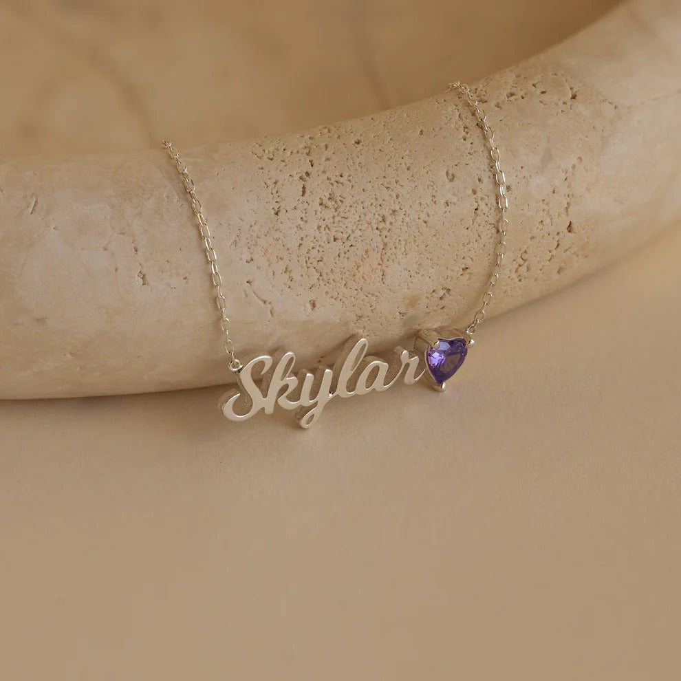 Gold necklace with 'Skylar' pendant on a beige stone surface