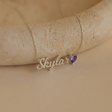 Gold necklace with 'Skylar' pendant on a beige stone surface