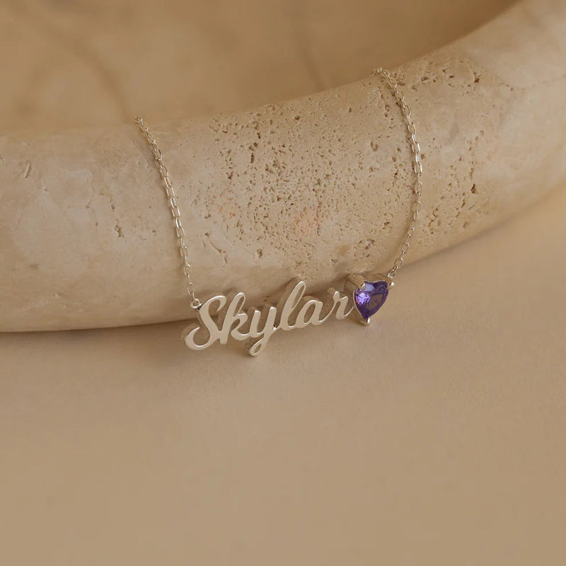 Gold necklace with 'Skylar' pendant on a beige stone surface