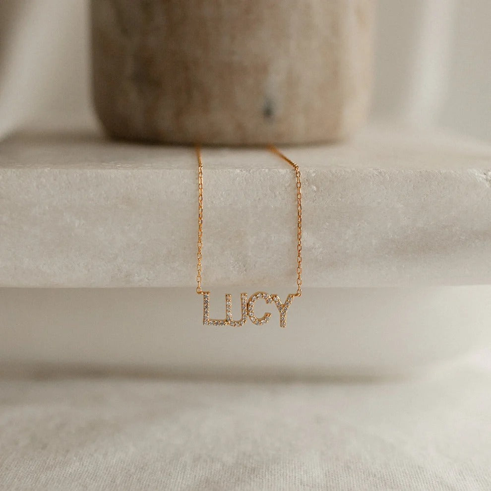 Gold necklace with 'LUCY' pendant on a neutral background