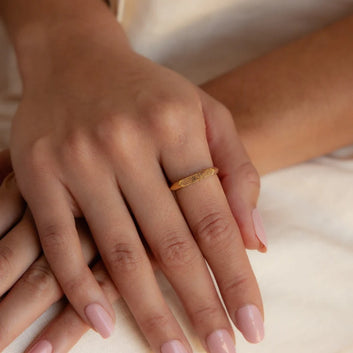 Close-up of a hand wearing a gold ring on a neutral background