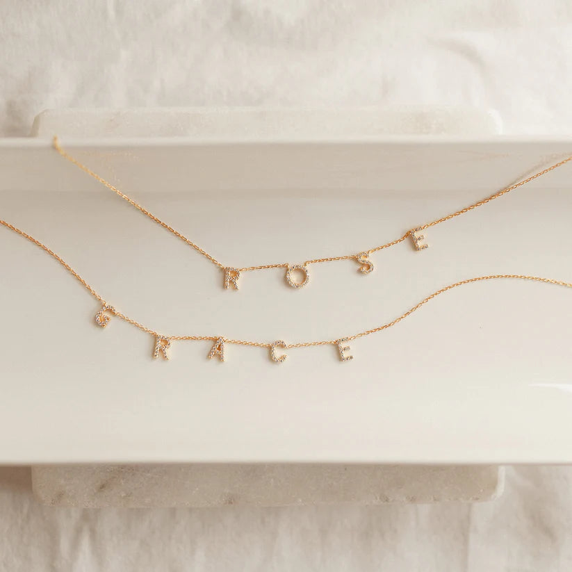 Gold necklace with letter pendants on a white surface