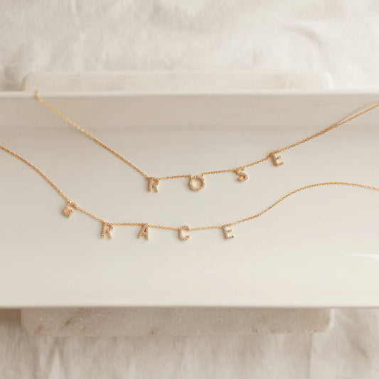 Gold necklace with letter pendants on a white surface