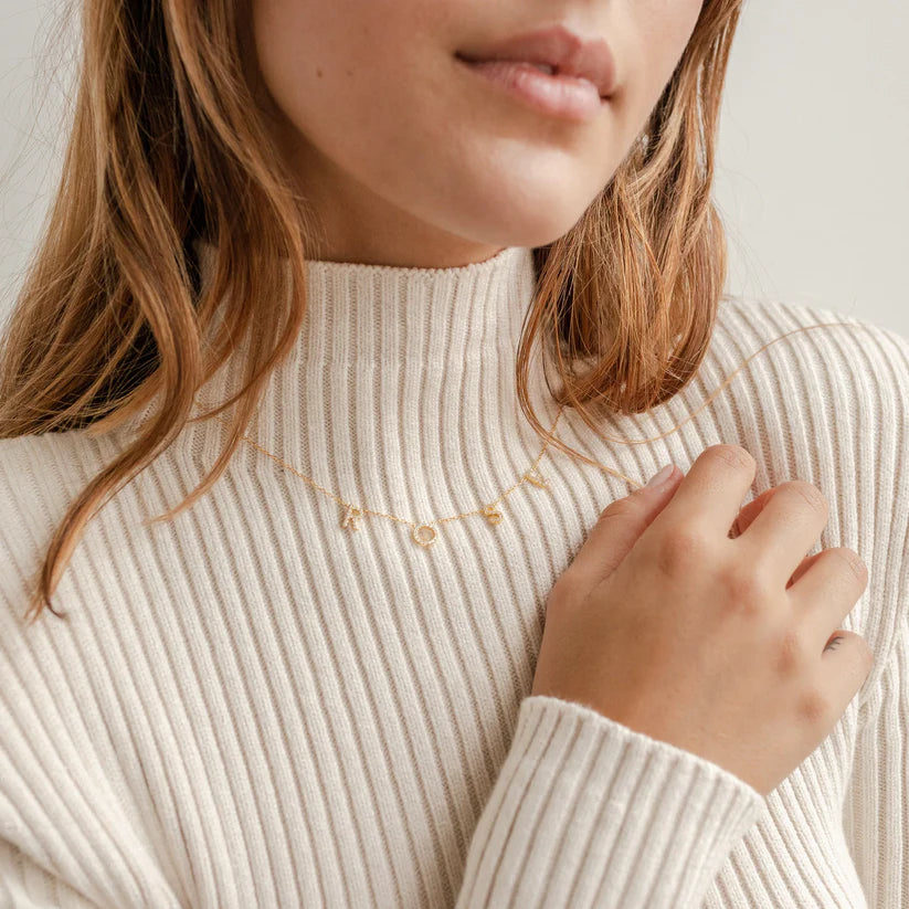 Close-up of a person wearing a beige ribbed sweater with a gold necklace.