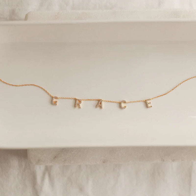 Gold necklace with letter charms spelling 'FAKE' on a white surface