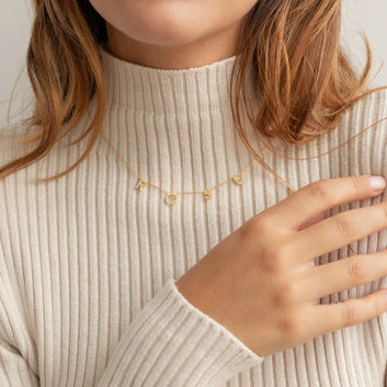 Person wearing a gold necklace with small pendants against a neutral background