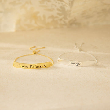 Two gold bracelets with engraved messages on a beige background