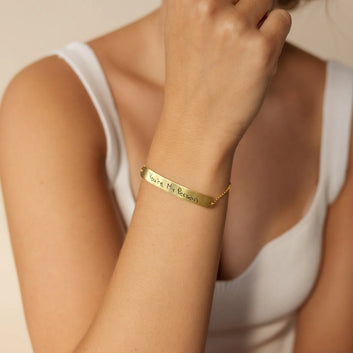 Gold bracelet with engraved message on a person's wrist against a neutral background