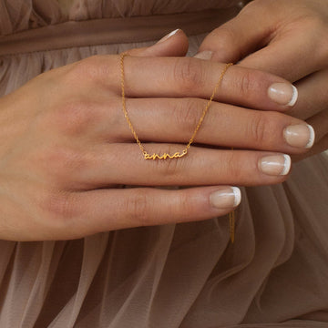 Gold ring with 'anna' engraving on a hand against a soft brown background