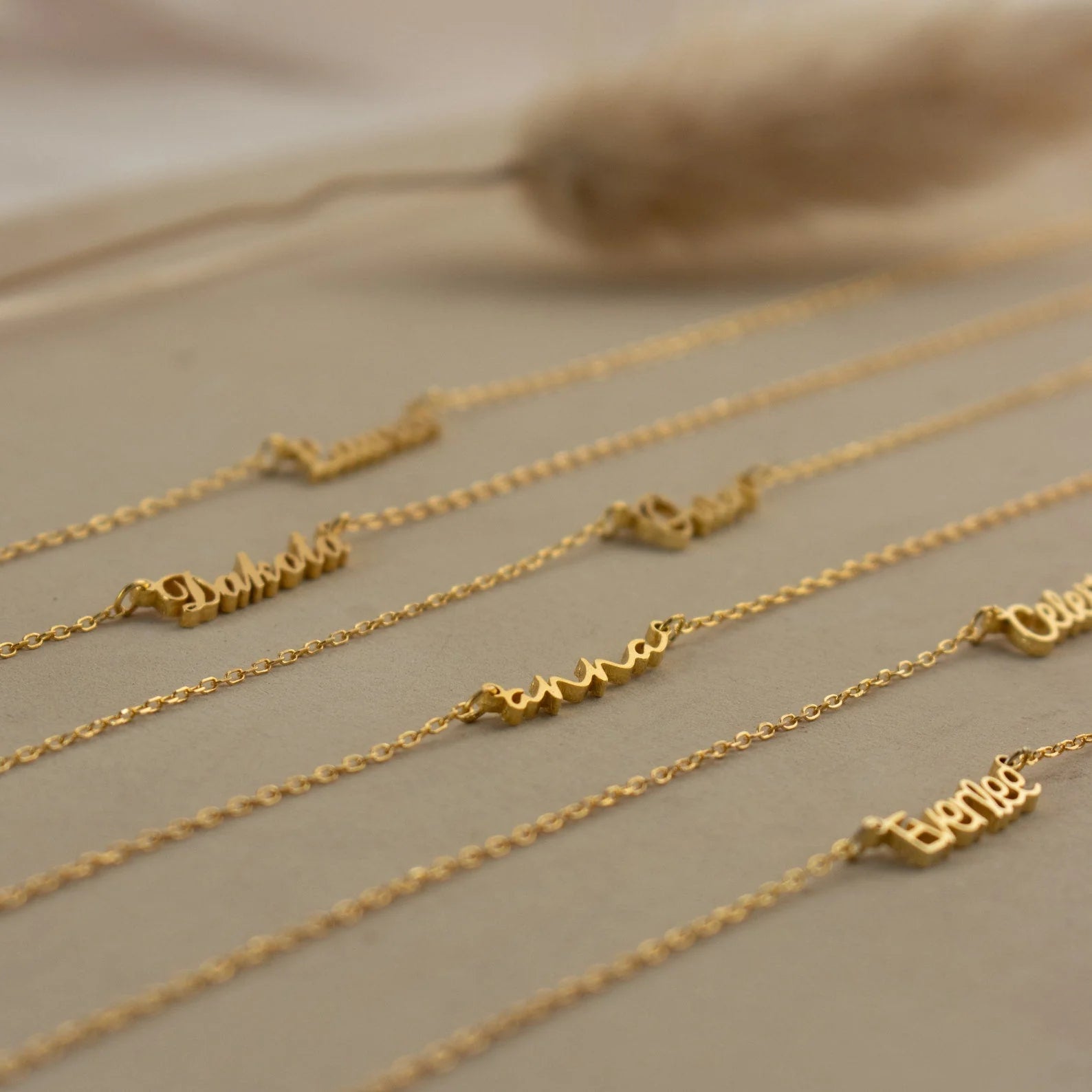 Gold necklaces with engraved names on a neutral background