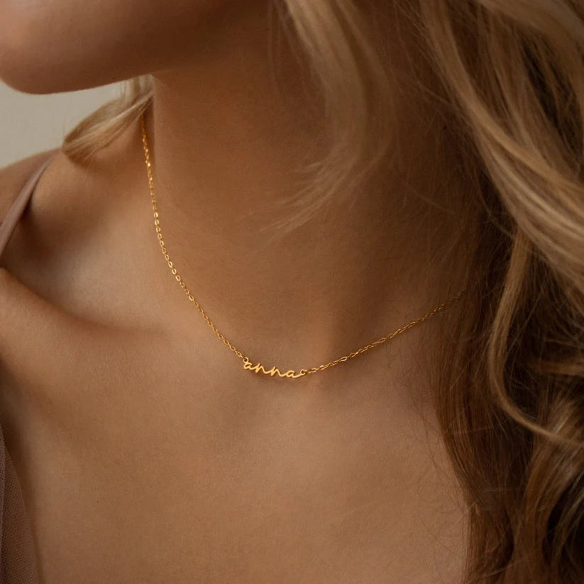 Gold necklace with a name on it worn by a person with blonde hair.