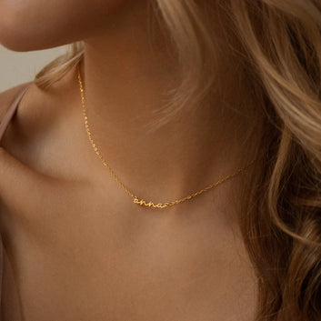Gold necklace with a name on it worn by a person with blonde hair.