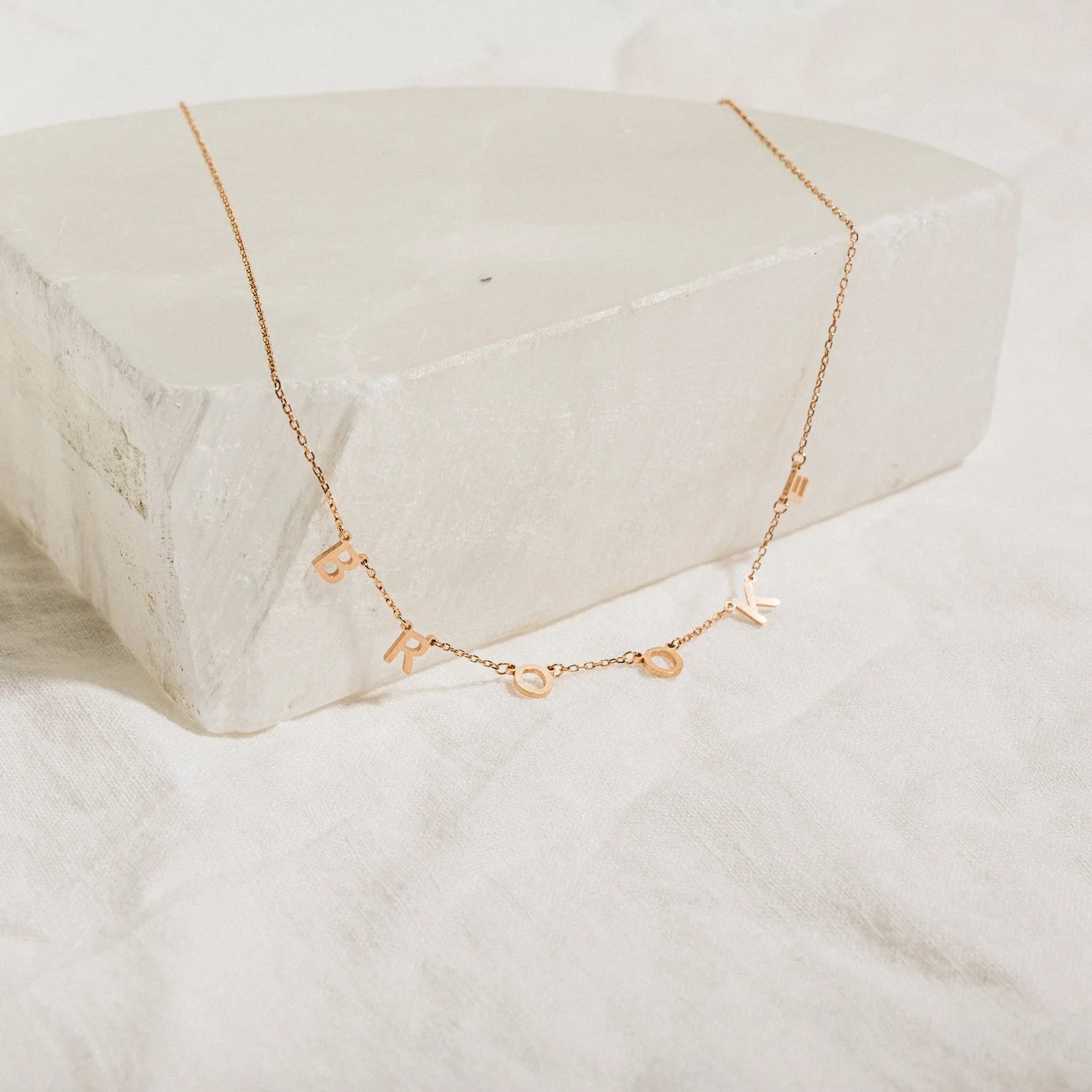 Rose gold necklace with small pendants on a white stone surface