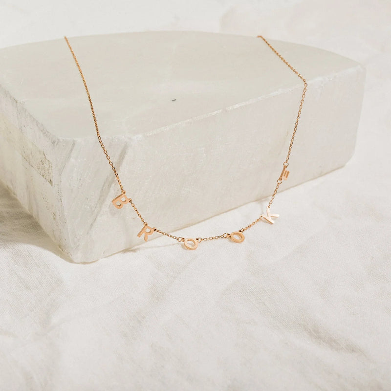 Rose gold necklace with small pendants on a white stone surface