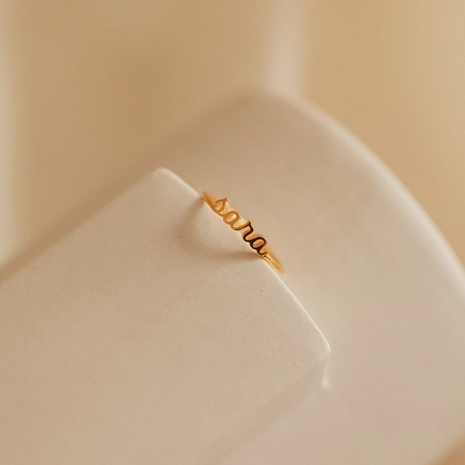 Gold ring with 'sara' engraving on a beige background