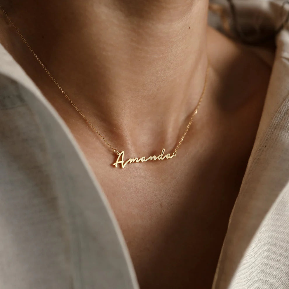 Gold necklace with 'Amanda' pendant on a person wearing a light-colored shirt.