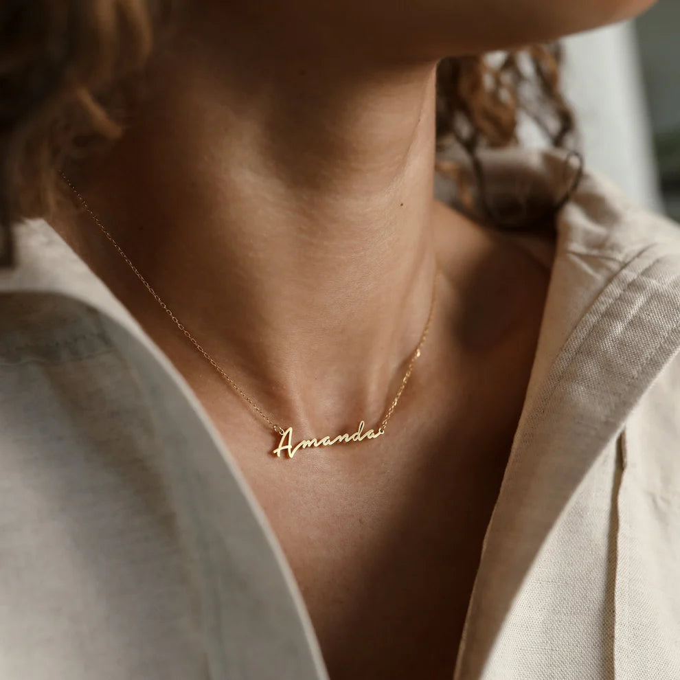 Gold necklace with 'Amanda' pendant on a person wearing a light-colored shirt.