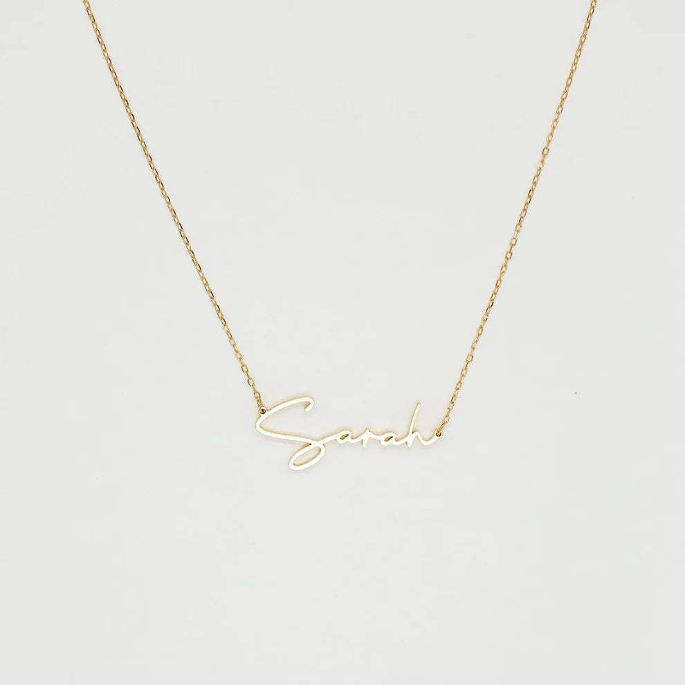 Gold necklace with 'Sarah' pendant on a light gray background