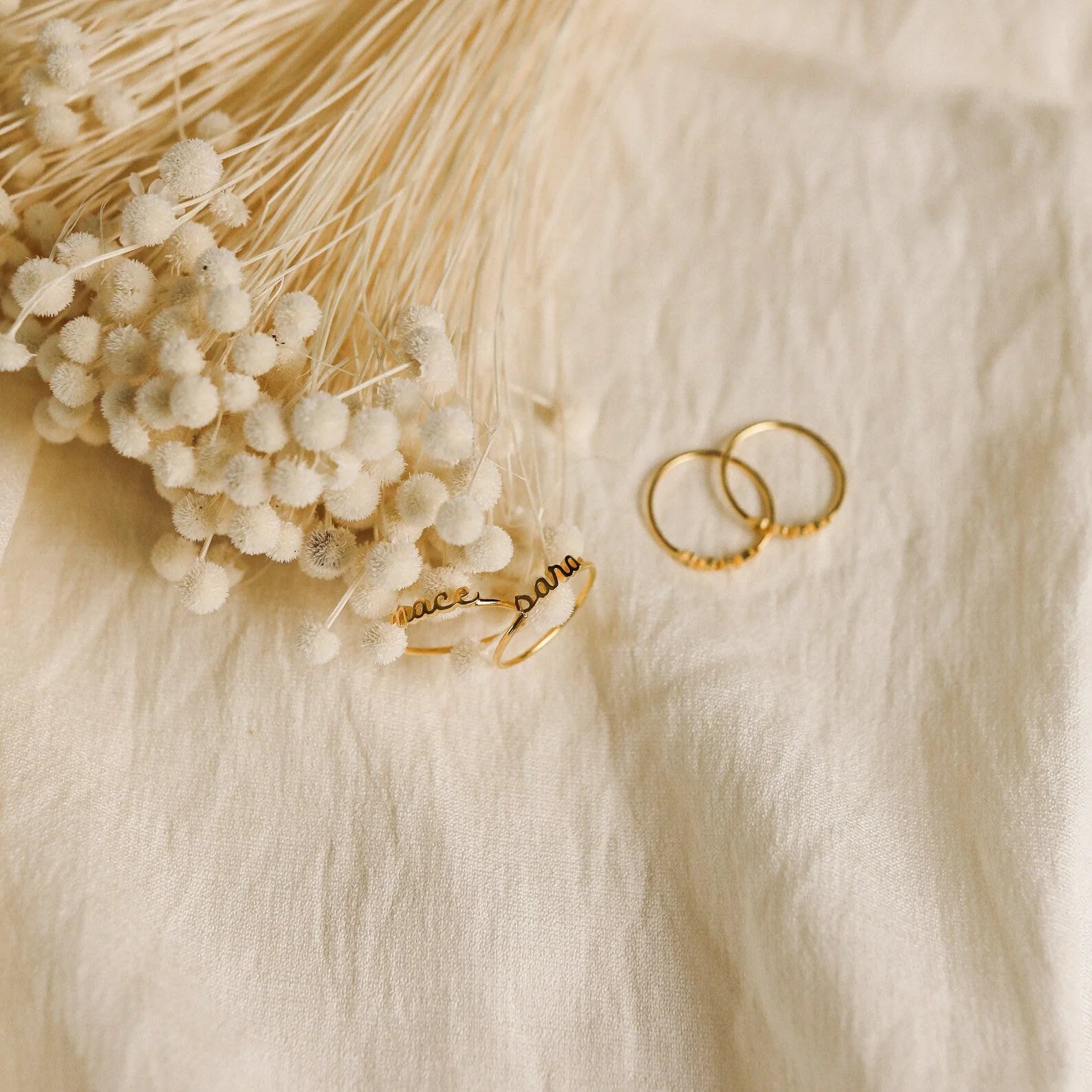 Gold rings on a textured beige surface with dried flowers