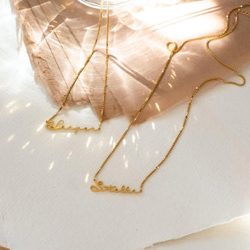 Gold necklaces with engraved names on a light background
