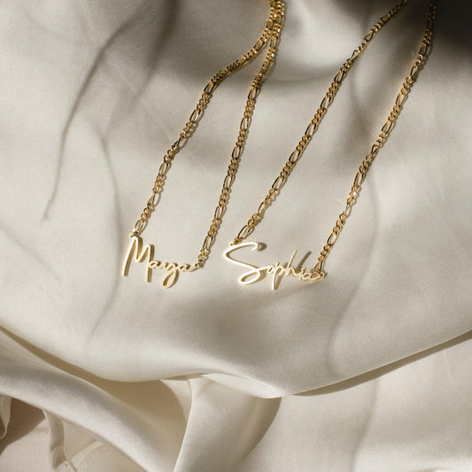 Two gold name necklaces on a soft fabric background