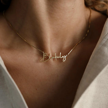 Gold necklace with 'Blakely' pendant on a person wearing a light-colored top.