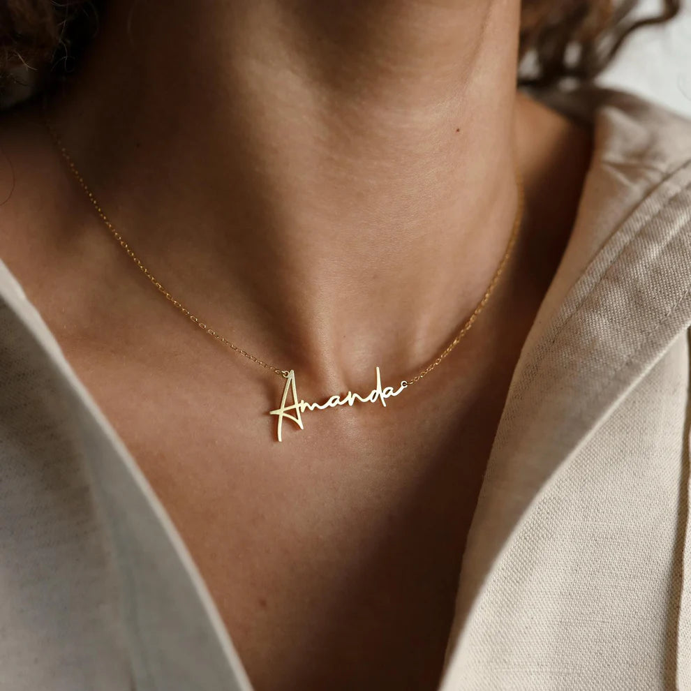 Gold necklace with 'Amanda' pendant on a person wearing a beige top.
