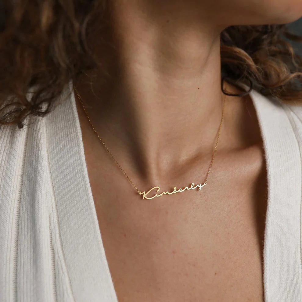Gold necklace with 'Kimberly' pendant on a person wearing a white top.
