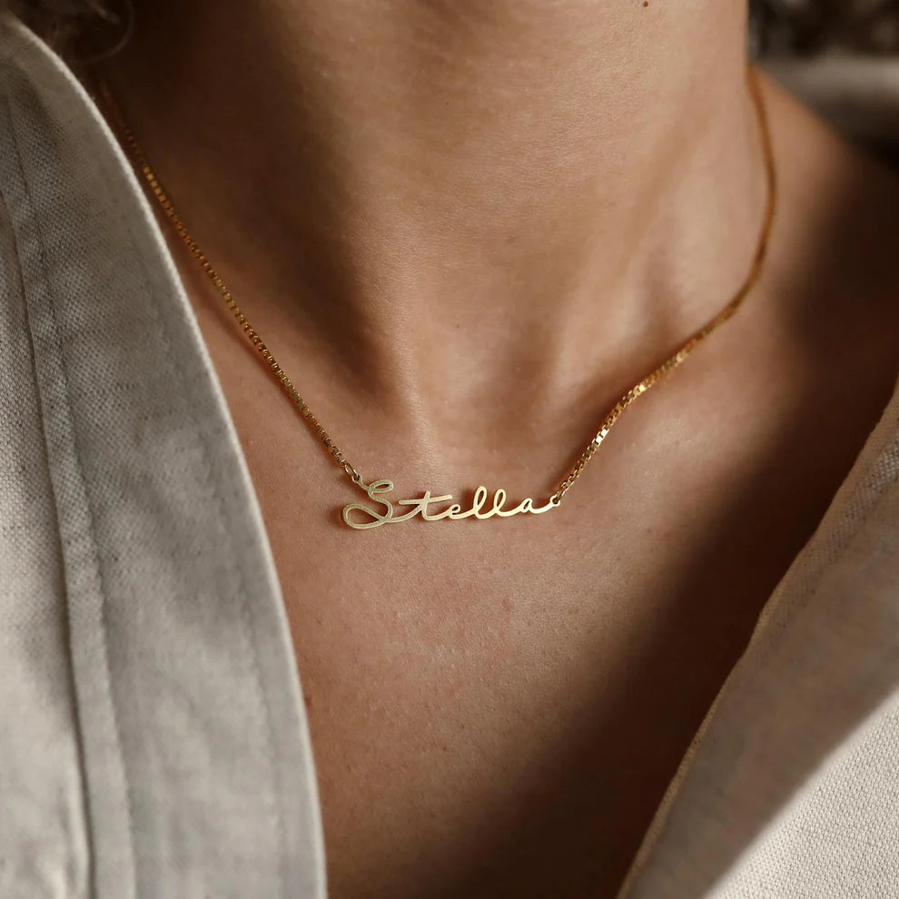 Gold necklace with 'Stella' pendant on a person wearing a light gray shirt.