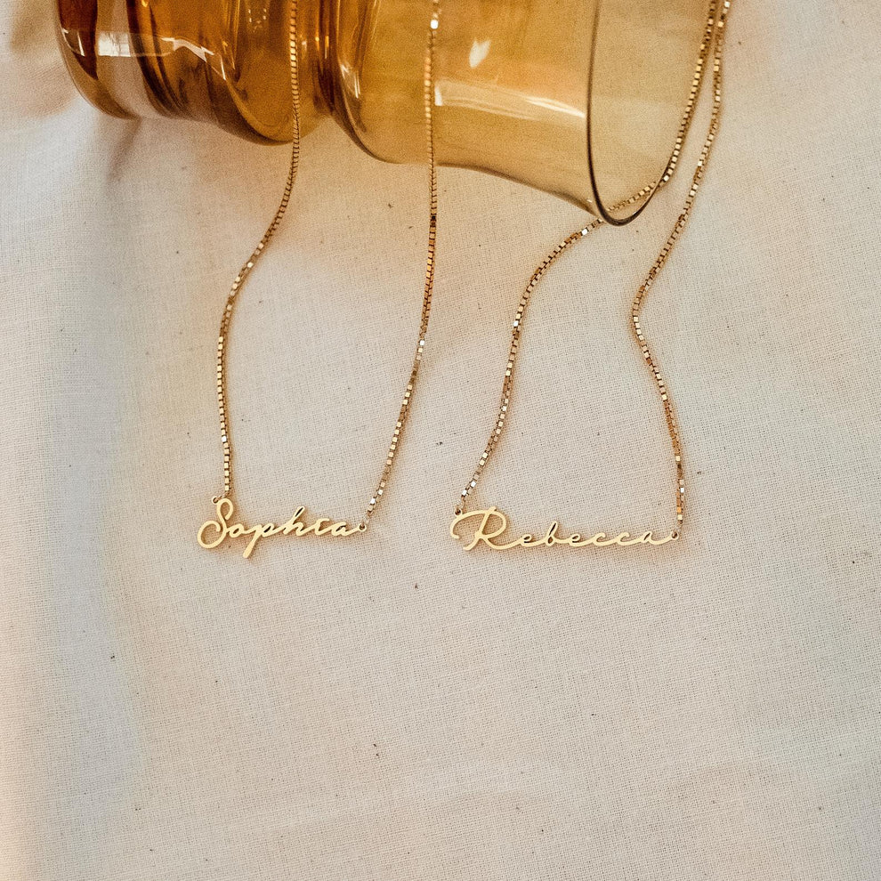 Two gold name necklaces, 'Sophia' and 'Rebecca', on a light background.
