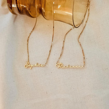 Two gold name necklaces, 'Sophia' and 'Rebecca', on a light background.