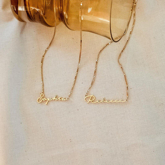 Two gold name necklaces, 'Sophia' and 'Rebecca', on a light background.