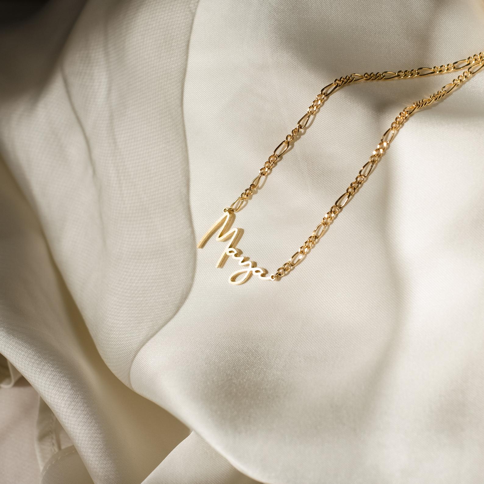 Gold necklace with 'Mrs.' pendant on a beige fabric background