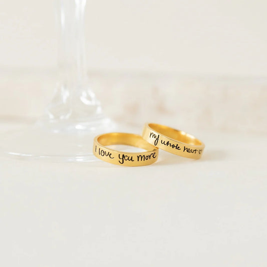 Two gold rings with engraved text on a white background